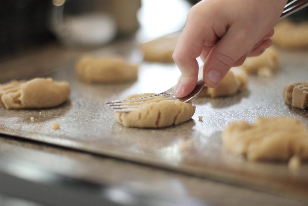 Mão segurando uma colher amassando a massa de um biscoito como exemplo de culinária infantil