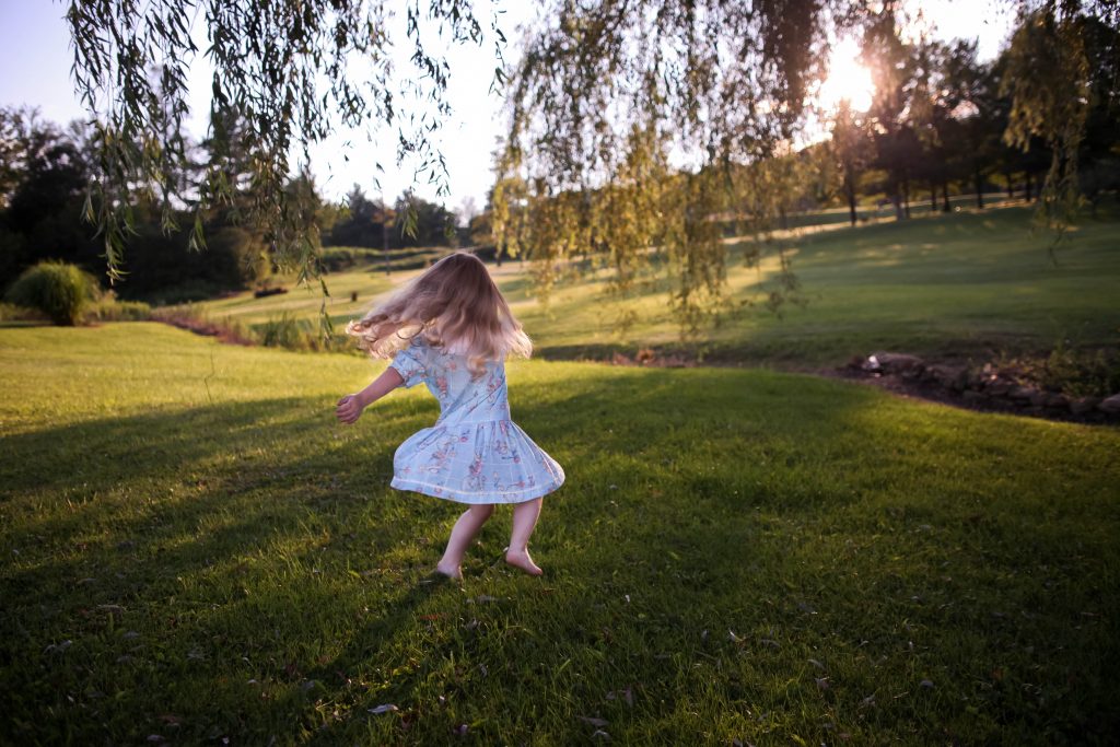 Criança menina dançando em um campo verde, demonstrando a importância da psicomotricidade infantil.