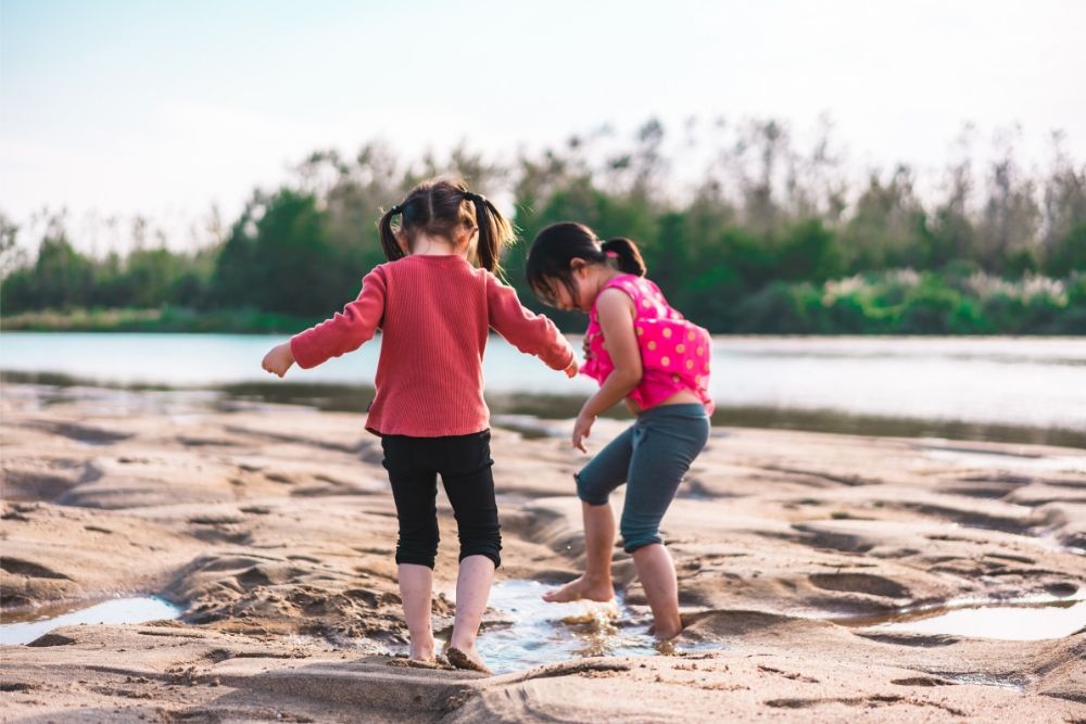 Duas crianças meninas experienciando percepção sensorial ao brincar em poças de água.