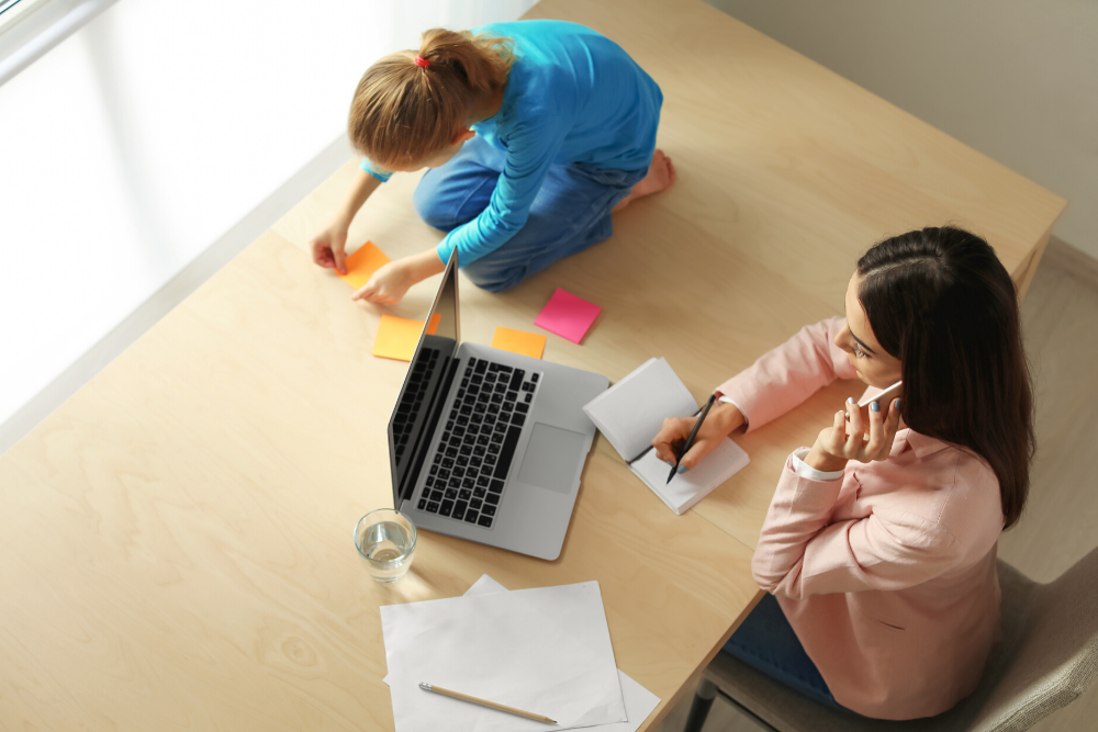 Mãe trabalhando em casa enquanto a filha brinca com post-its