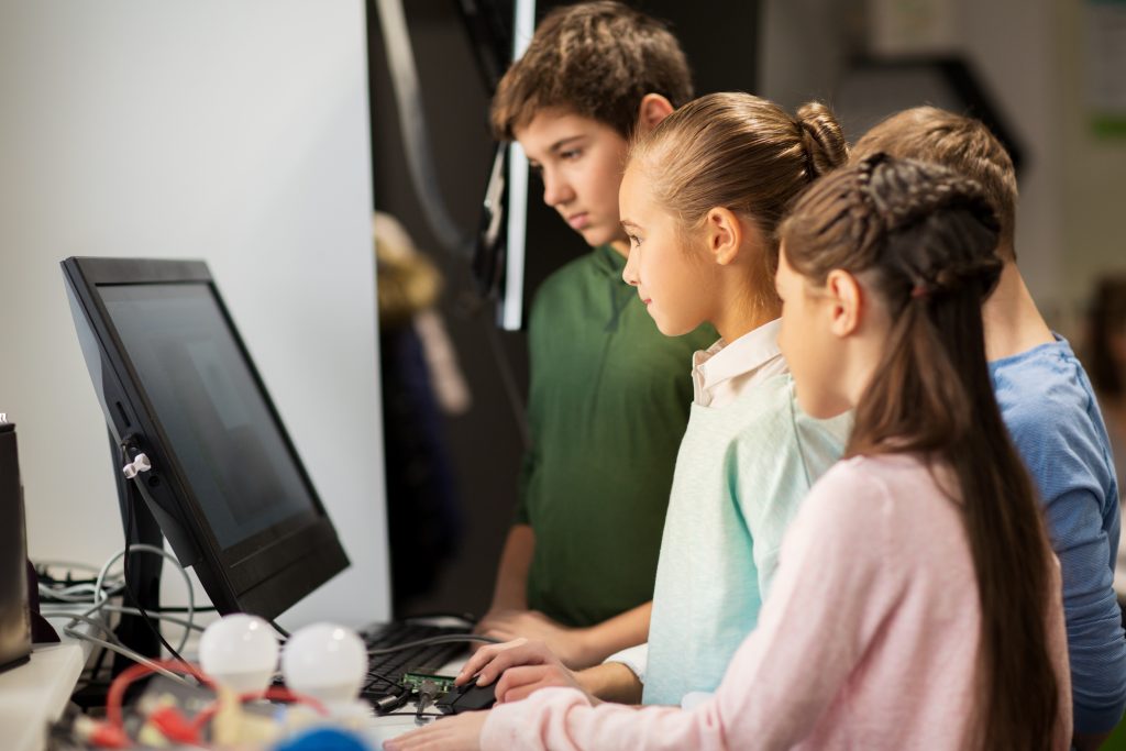 Crianças usando um computador em sala de aula, demonstrando a tecnologia na educação.