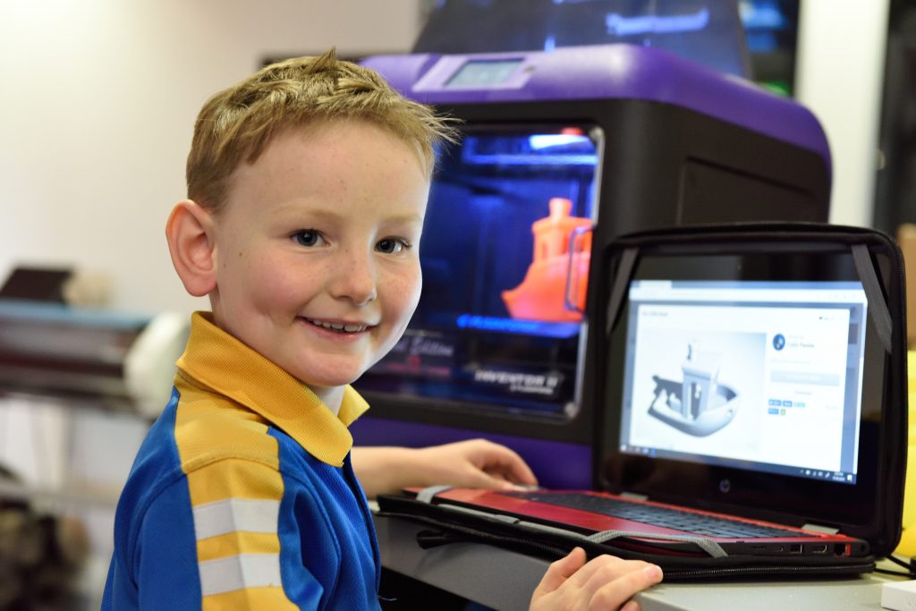 Menino criança usando um computador em sala de aula, demonstrando tecnologia na educação.