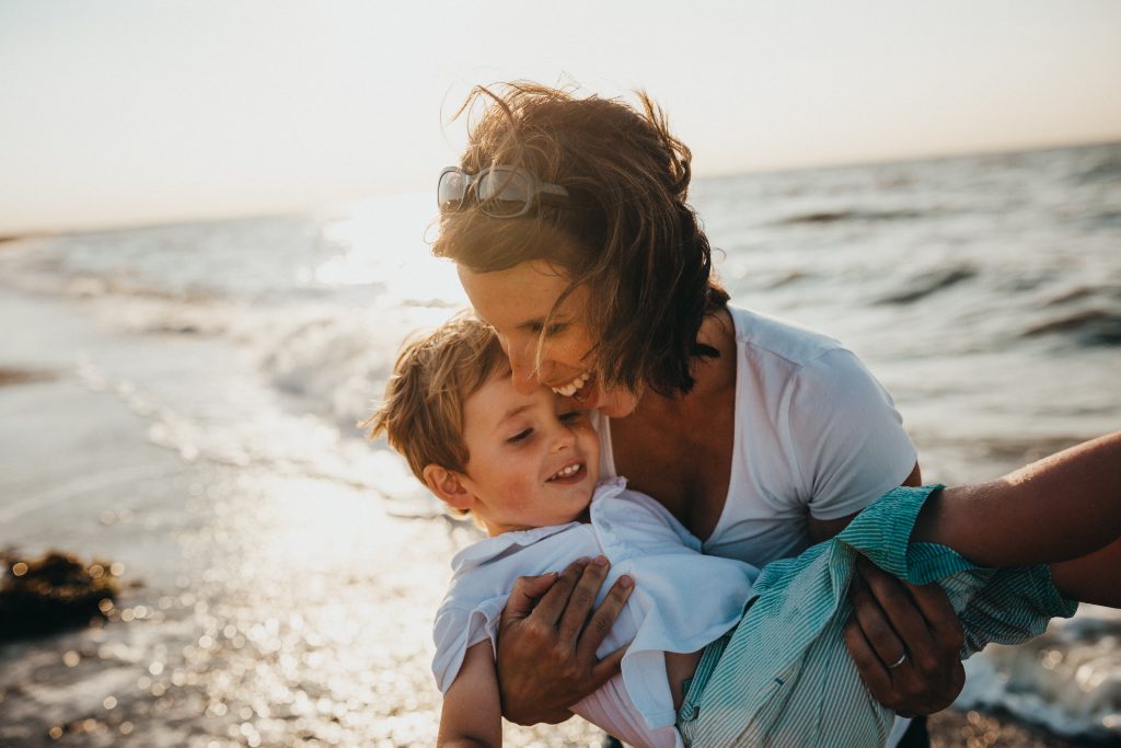 Mãe brincando com seu filho no mar, exemplificando a importância do afeto no desenvolvimento da criança.